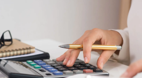 main qui tient un stylo au dessus d'une calculette