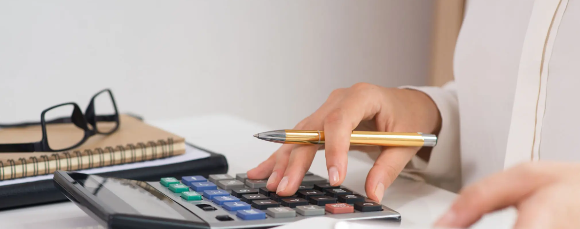 main qui tient un stylo au dessus d'une calculette